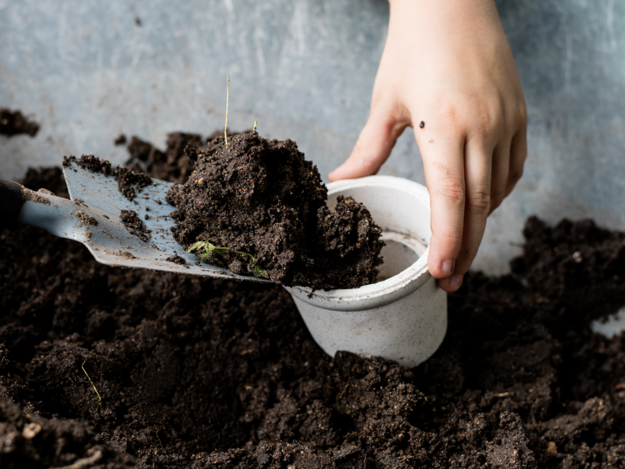 Hand with a shovel putting potting soil into a container. 
